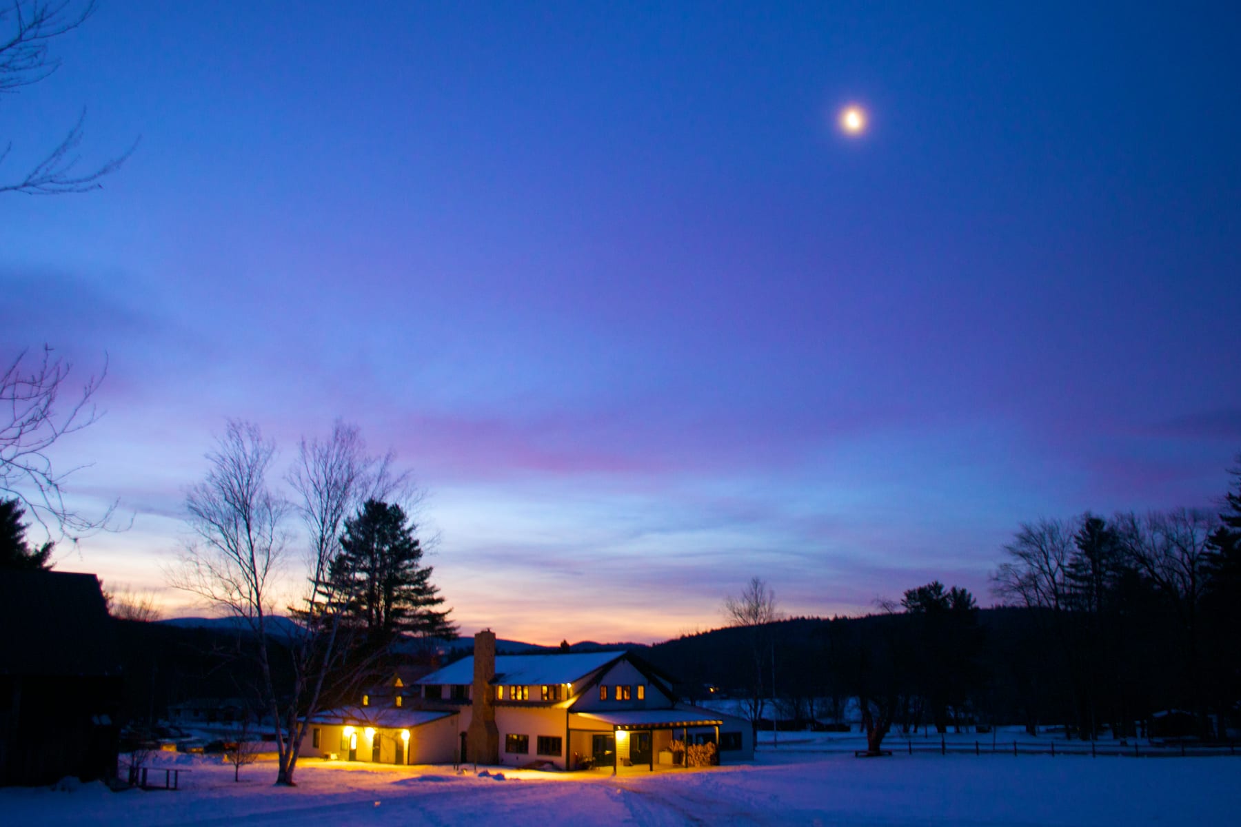Hulbert main hall illuminated at night with snow on the ground and a moon in the sky.